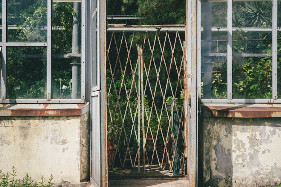 A brick-built outdoor alcove set into a stone wall, housing two metal watering cans with long spouts, one darker and aged, the other slightly lighter and newer. The area features a small, round, white